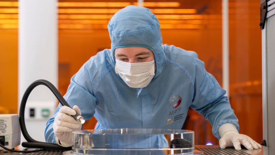 Technical officers manoeuvre glass substrate prior to polishing in the ANU Research School of Physics cleanroom.